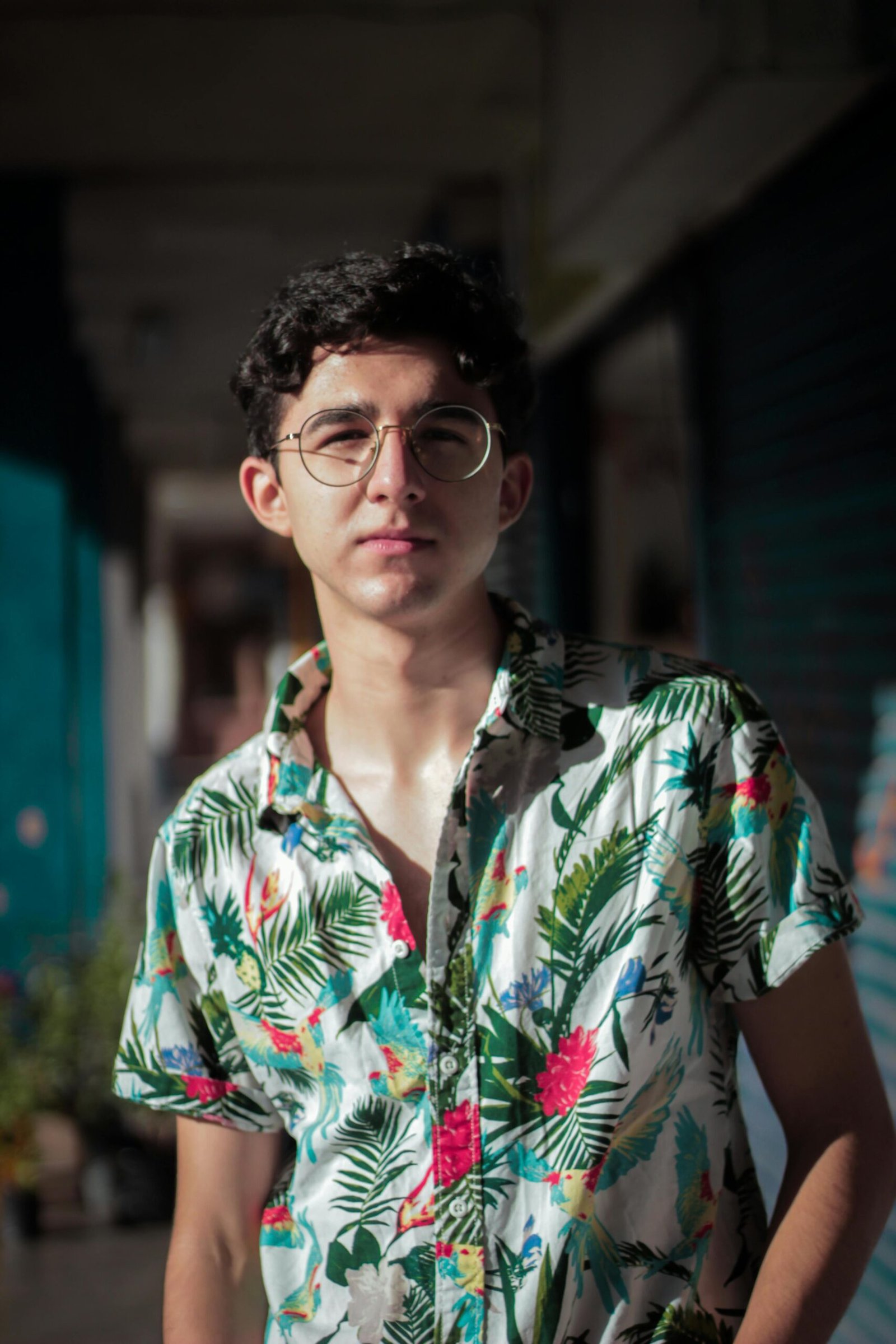 Portrait of a young man wearing a floral shirt and eyeglasses outdoors in sunlight.